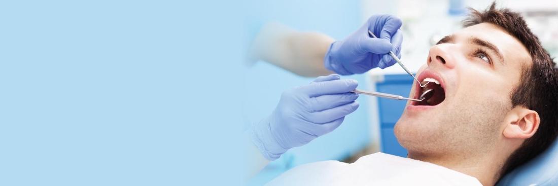 young brown haired man being examined by dentist in blue gloves