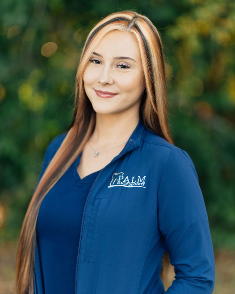 Lexi, Front Office Administrator at Palm Family Dentistry, smiling outdoors in a blue branded jacket