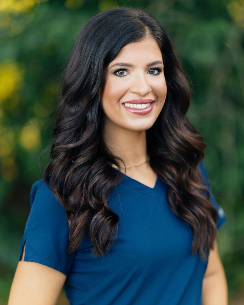 Paige, dental insurance coordinator, smiling warmly in blue scrubs outdoors