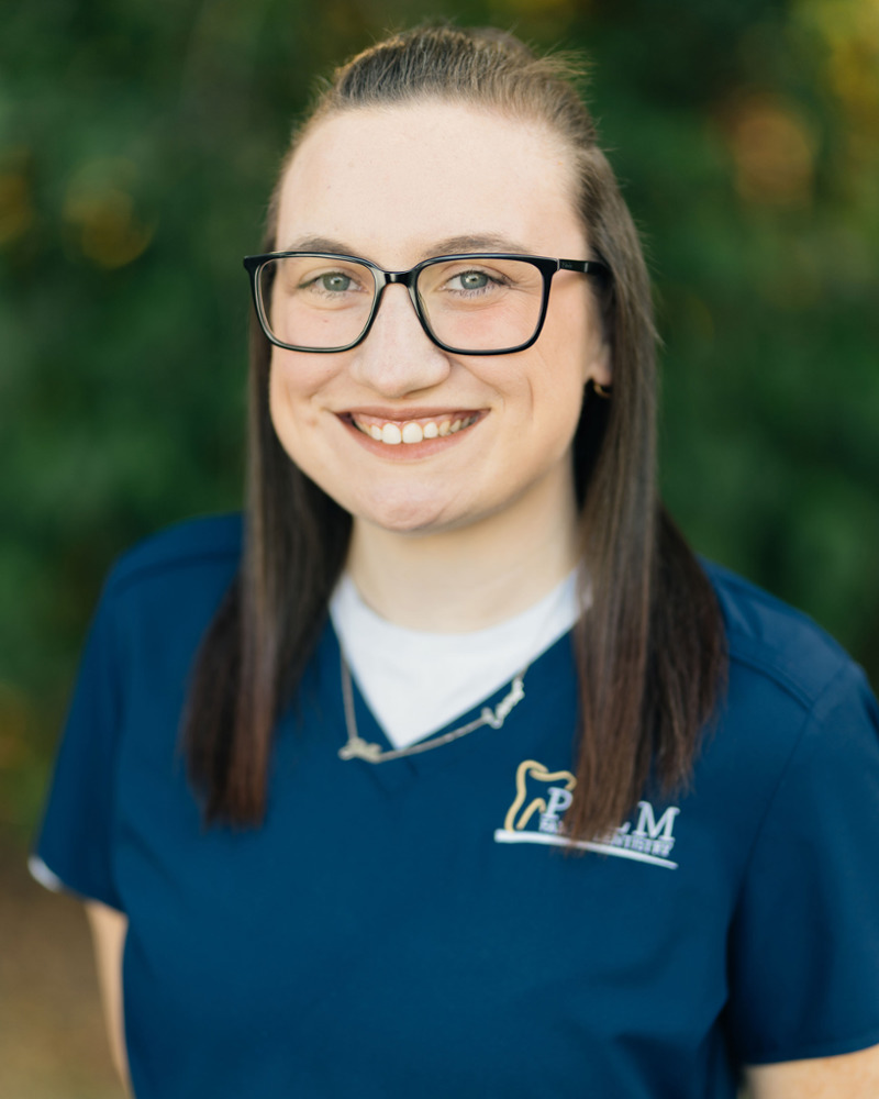 Kim, dental assistant at Palm Family Dentistry, smiling in navy scrubs with glasses outdoors